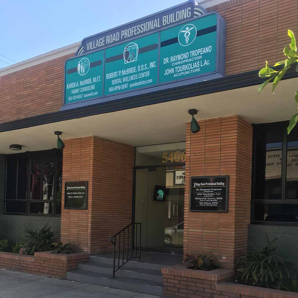 Exterior of a neighborhood health and wellness clinic building on a tree-lined Southern California street, warm afternoon light, welcoming storefront, professional signage, photorealistic